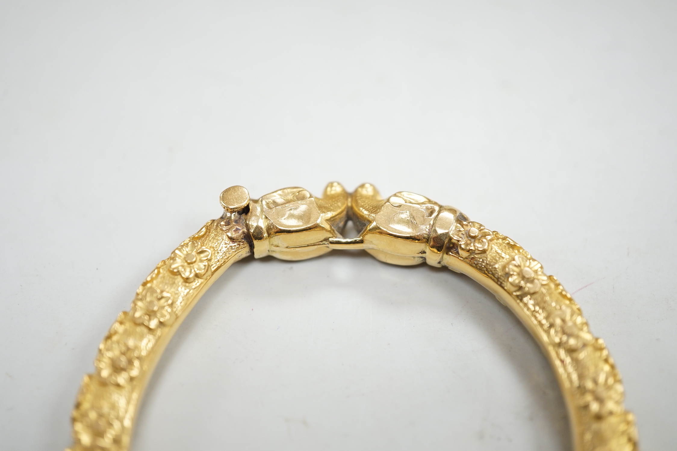 An antique yellow metal hinged bangle, with flower head decoration and dragon's? head terminals, gross weight 23.9 grams.